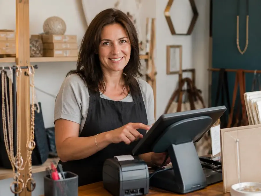 Commerçante souriante qui encaisse sur une caisse enregistreuse tactile certifiée NF525 dans sa boutique